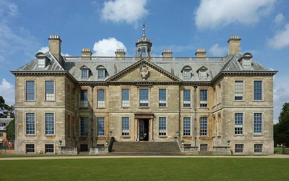 Belton House south front with entrance steps and a lawn beneath a blue sky