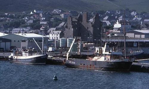 Fishing boats moored in Scalloway harbour with the castle behind