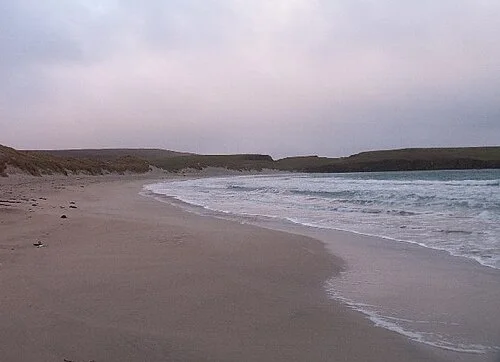 Waves breaking along Scousburgh Sands beneath a pale sky